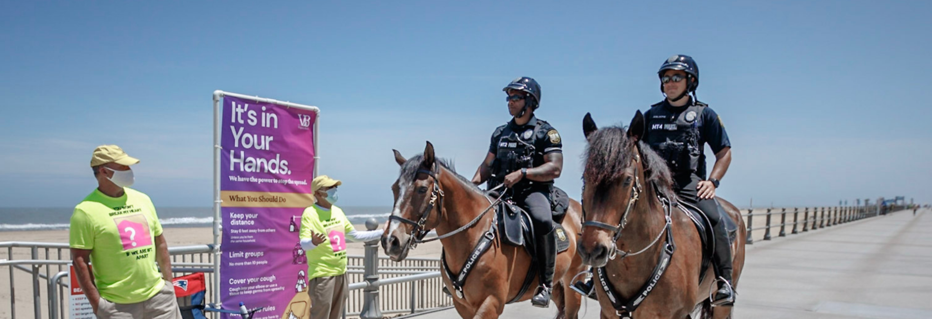 Two mounted patrol officers riding horses along boardwalk talking to resident