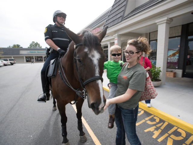 Mounted patrol polcie officer on horseback introducing horse to mother and child