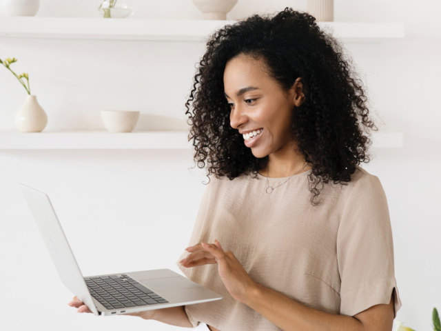 Woman in neutral colors smiling at her laptop Online Services Header